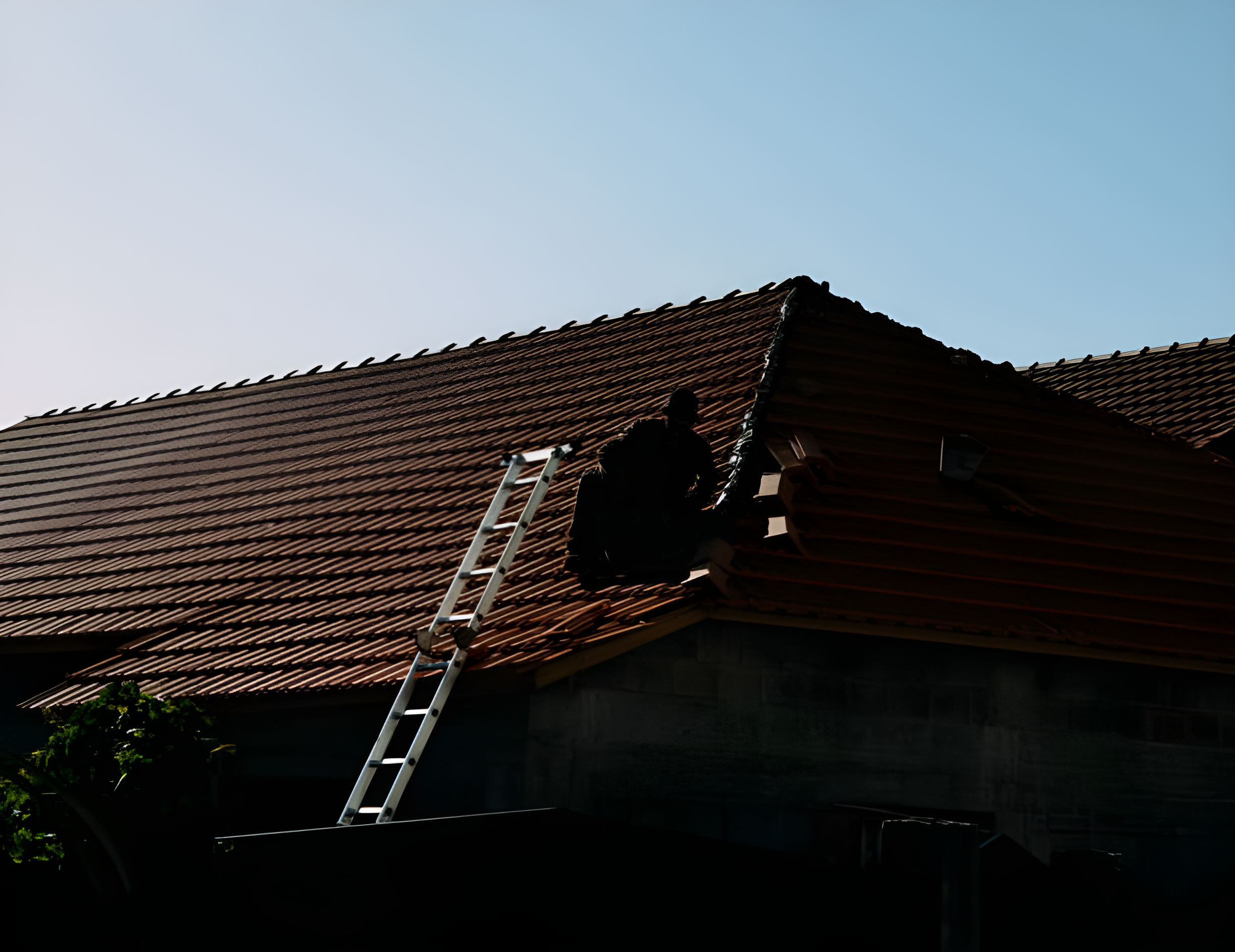 Roofing specialist working beside a ladder on a tiled roof